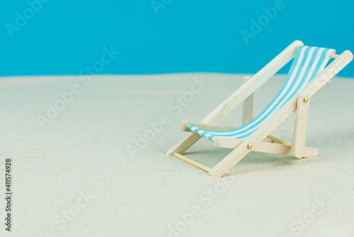 Beach relaxation and vacation concept. Toy sun lounger on sand and colorful paper background.