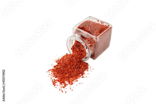 Fototapeta Naklejka Na Ścianę i Meble -  chilli pepper seedless flakes pouring out of a glass jar isolated on white background. Spices and food ingredients. in Korea known as Gochugaru. Used for Kimchi.