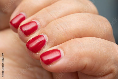 Lady's nails with bright red nail polish in which regrowth can be seen, concept of the need for a new manicure