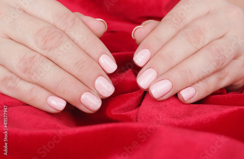 female hands with beautiful manicure and soft pink nail polish on a crumpled red velvet background.