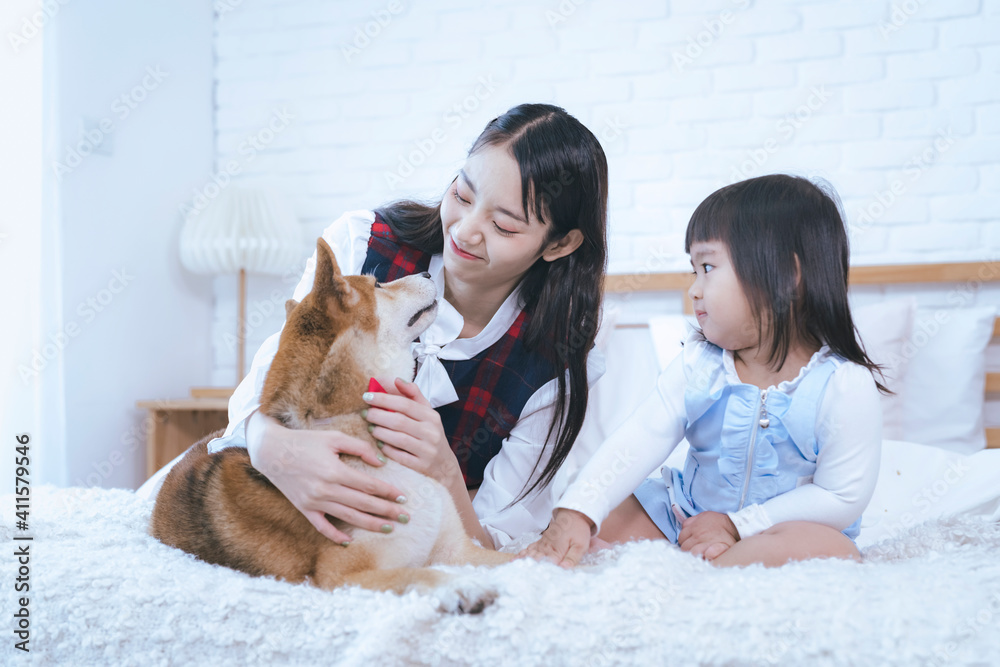 Young Asian women and girl were in bed with a dog. Shiba inu dog on the bed with two girl.