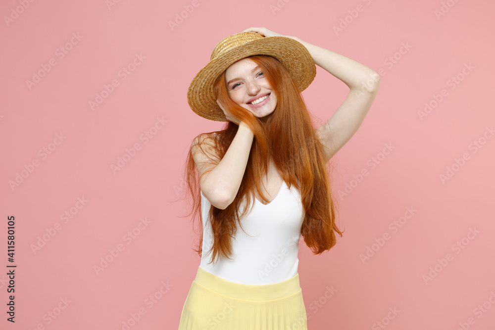 Young smiling atractive caucasian cute redhead woman 20s ginger long hair wearing straw hat summer clothes looking camera touching put hands on head isolated on pastel pink background studio portrait. Young smiling atractive caucasian cute redhead woman 20s ginger long hair wearing straw hat summer clothes looking camera touching put hands on head isolated on pastel pink background studio portrait.