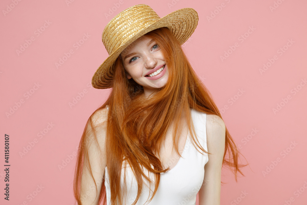 Young smiling atractive caucasian cute nice redhead woman 20s ginger long hair wearing straw hat summer clothes looking camera tilted head isolated on pastel pink color background studio portrait. Young smiling atractive caucasian cute nice redhead woman 20s ginger long hair wearing straw hat summer clothes looking camera tilted head isolated on pastel pink color background studio portrait.