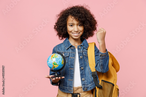Smiling little african kid school girl 12-13 years old in casual clothes backpack hold in palms Earth world globe do winner gesture clench fist isolated on pink background Childhood education concept.