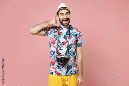 Excited young traveler tourist man in hat photo camera doing phone gesture says call me back isolated on pink background. Passenger traveling abroad on weekends getaway. Air flight journey concept.