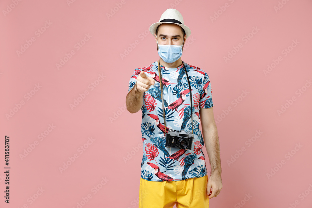 Funny traveler tourist man in face mask to safe from coronavirus virus covid-19 point index finger camera on youn isolated on pink background. Passenger travel on weekend. Air flight journey concept. Funny traveler tourist man in face mask to safe from coronavirus virus covid-19 point index finger camera on youn isolated on pink background. Passenger travel on weekend. Air flight journey concept.