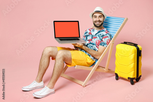 Fotótapéta Full length smiling traveler tourist man in hat sit on deck chair hold laptop pc computer with blank empty screen isolated on pink background