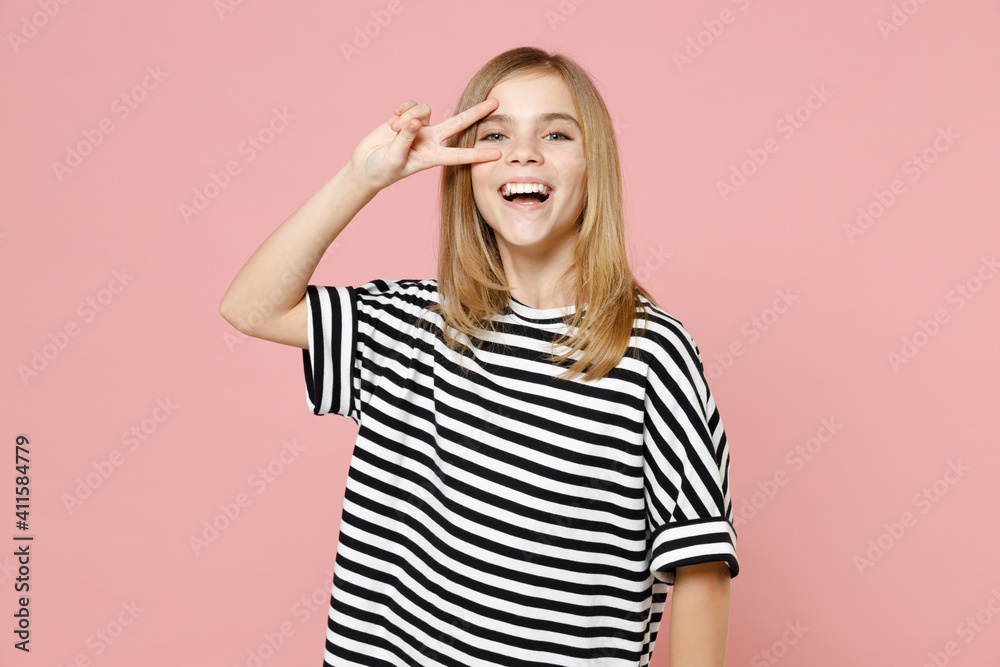 Little blonde smiling kid girl 12-13 years old wearing striped oversized t-shirt cover eye with victory v-sign gesture isolated on pastel pink background children studio . Childhood lifestyle concept. Little blonde smiling kid girl 12-13 years old wearing striped oversized t-shirt cover eye with victory v-sign gesture isolated on pastel pink background children studio . Childhood lifestyle concept.