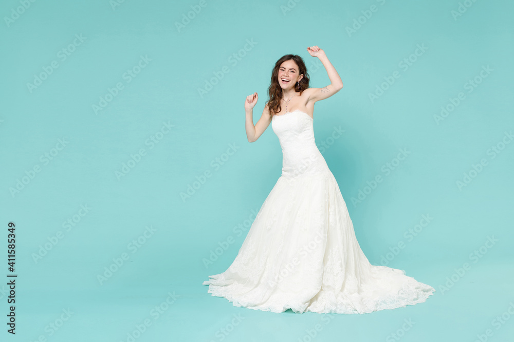 Full length of joyful bride young woman in white wedding dress doing winner gesture clenching fists dancing isolated on blue turquoise background studio portrait. Ceremony celebration party concept. Full length of joyful bride young woman in white wedding dress doing winner gesture clenching fists dancing isolated on blue turquoise background studio portrait. Ceremony celebration party concept.