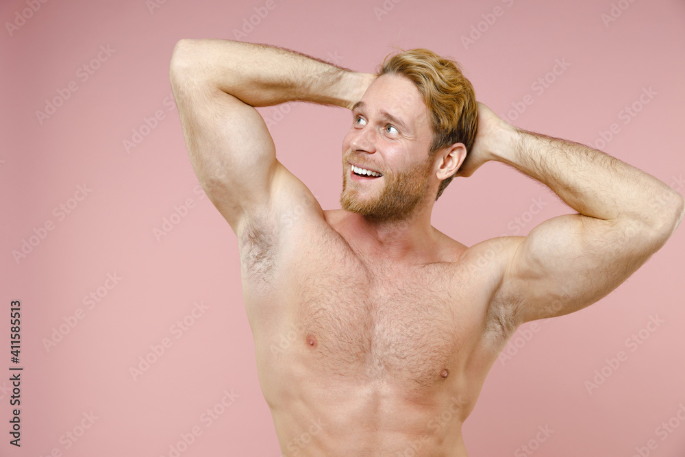 Funny bearded naked young man 20s years old perfect skin holding hands behind head looking aside isolated on pastel pink background studio portrait. Skin care healthcare cosmetic procedures concept.