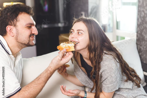 Happy couple at home feeding each other with pizza  dating at home. Care and love concept.