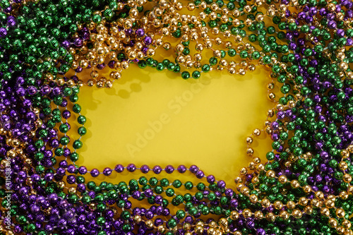 A frame of three colors of Mardi gras beads on yellow background