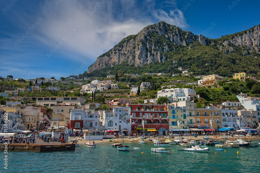 Small fishing boats at harbor Marina Grande in Capri. View from the sea of Marina Grande harbor, with colorful buildings and high mountains in the background, Capri Island, Tyrrhenian sea, Italy