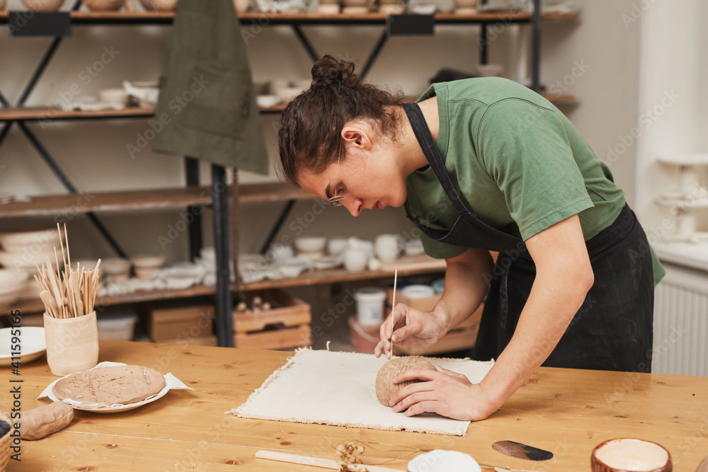 Side view portrait of young man decorating ceramic bowl in pottery workshop, hobby and small business concept, copy space Side view portrait of young man decorating ceramic bowl in pottery workshop, hobby and small business concept, copy space