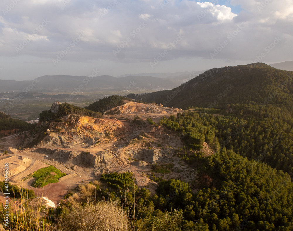 Aerial views of a quarry in the mountains, with a cloudy sky at sunset.