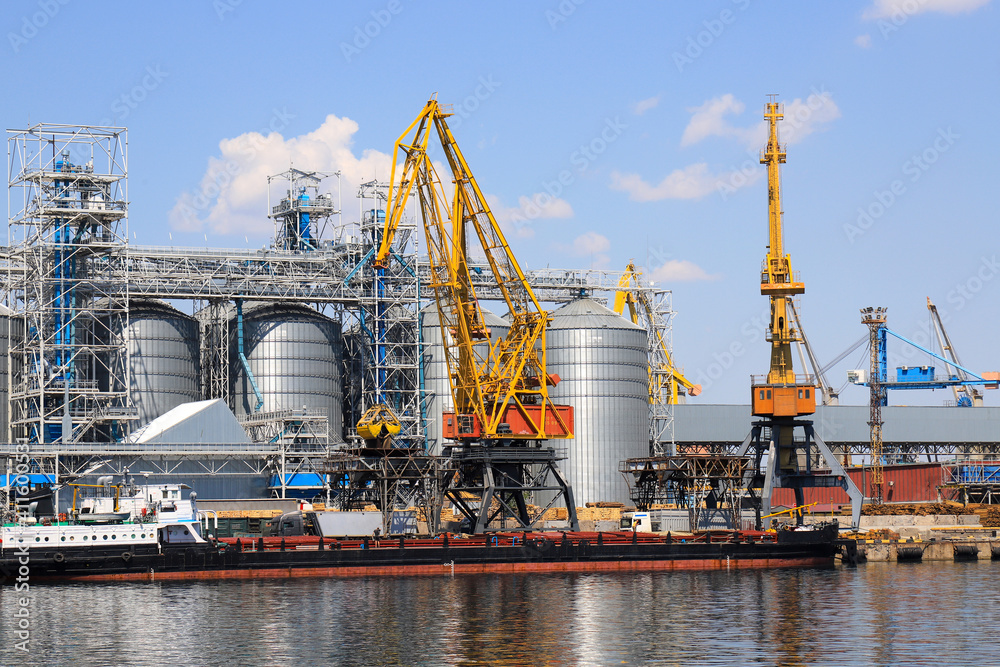 Big port at sea, harbor, pier by the water. Yellow harbor cranes unload a barge at the Odessa seaport among large metal tanks. Delivery, unloading of ships, transport, Odesa.
