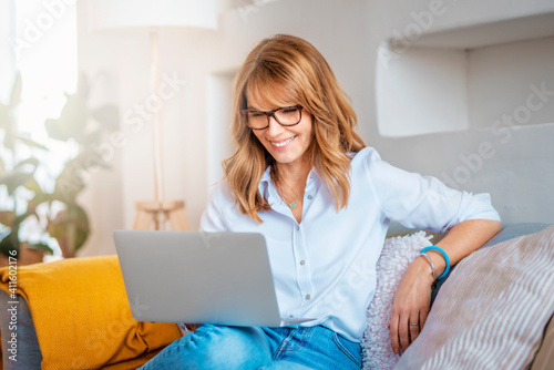 Shot of a middle aged woman using a laptop on the sofa at home. Businesswoman working from home.