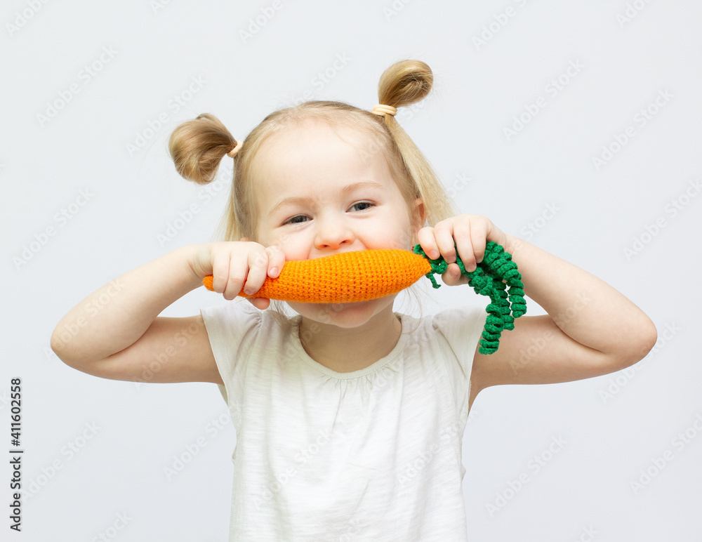 Little girl is eating toy knitt carrots healthy food on the white background Little girl is eating toy knitt carrots healthy food on the white background