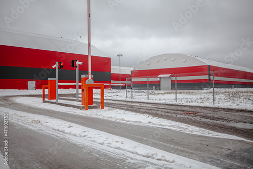 General shot of the industrial zone with red hangars and red checkpoint with barrier, covered with grey snow, in a gloomy, cold light, in winter