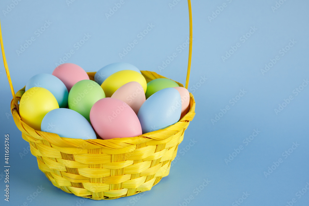 Easter eggs in a yellow basket with copy space for text on blue background.