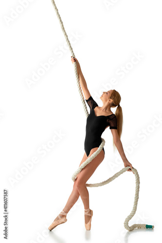 beautiful graceful ballerina in pointe shoes and black bodysuit is posing with rope on white studio background