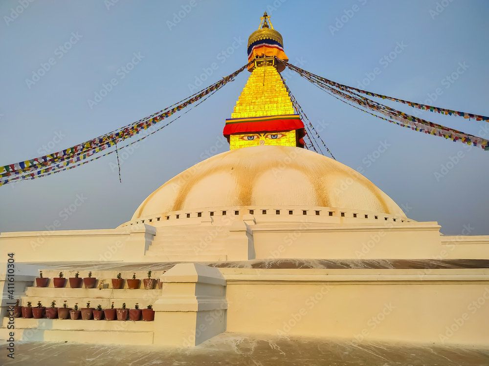 View of Boudhanath Stupa (or Bouddha Stupa) in the rays of the setting sun in Kathmandu city, Nepal. Prayer flags wings on the wind. No people. Religious architecture theme.