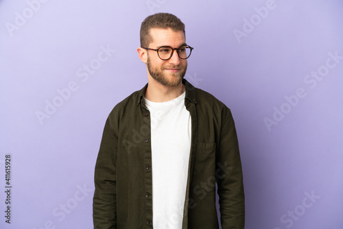 Young handsome caucasian man isolated on purple background having doubts while looking side