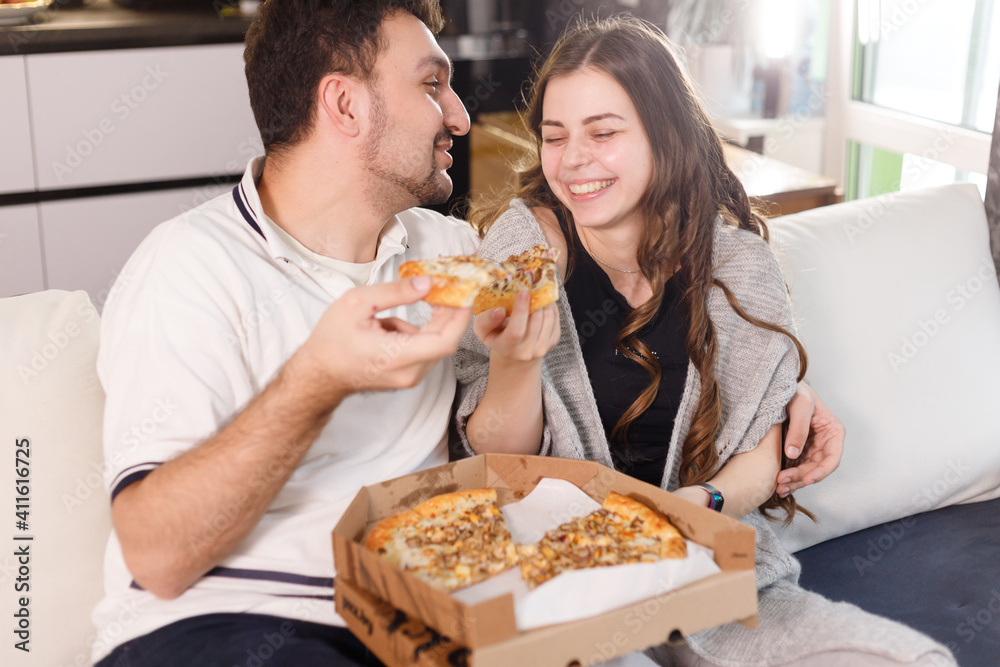 Happy couple at home feeding each other with pizza, dating at home. Care and love concept. Happy couple at home feeding each other with pizza, dating at home. Care and love concept.