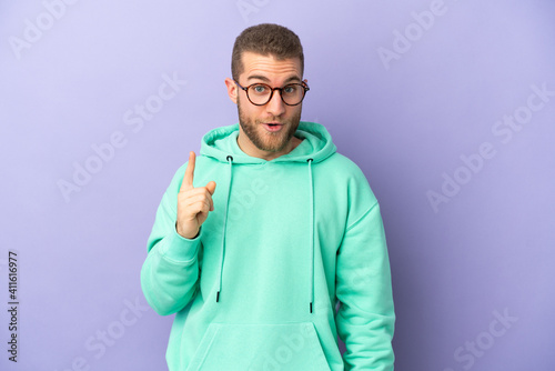 Young handsome caucasian man isolated on purple background intending to realizes the solution while lifting a finger up © luismolinero
