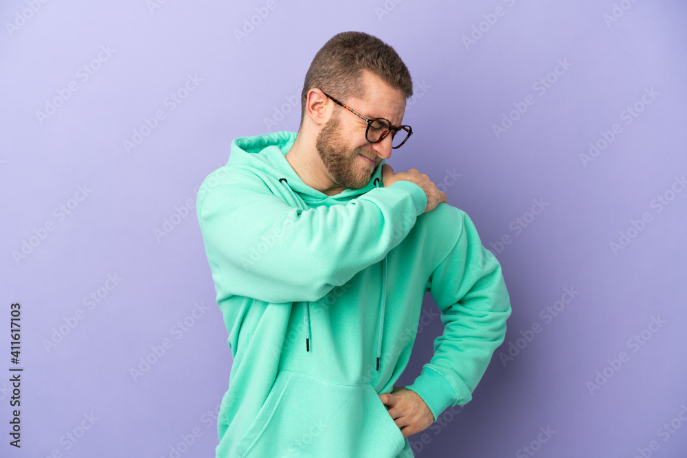 Young handsome caucasian man isolated on purple background suffering from pain in shoulder for having made an effort Young handsome caucasian man isolated on purple background suffering from pain in shoulder for having made an effort