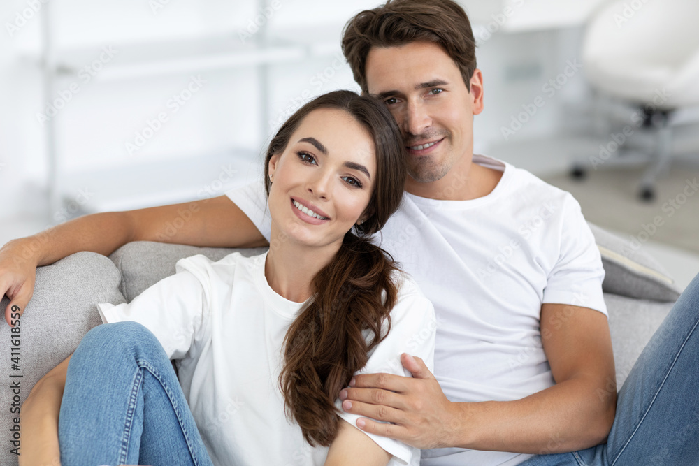 Happy couple i in love siting on a cozy sofa at home. Hugging and looking at camera. Happy couple i in love siting on a cozy sofa at home. Hugging and looking at camera.