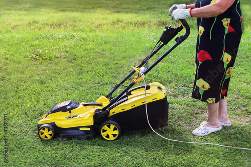 Elderly lady pushing an electric mower to cut the grass. Active seniors are passionate about their hobbies and lead meaningful quiet lives