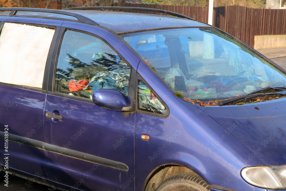 The detail of an abandoned broken car, now a wreck with damaged or broken windows and full of rubbish or waste. Occupies a parking place for the others.  