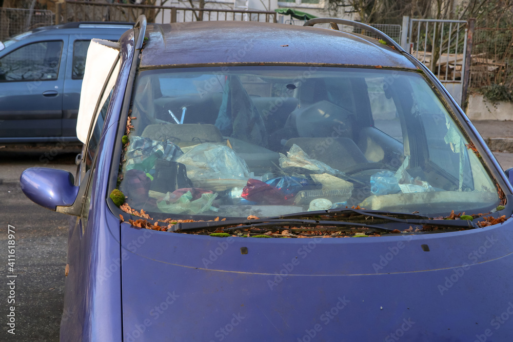 Obraz premium The detail of an abandoned broken car, now a wreck with damaged or broken windows and full of rubbish or waste. Occupies a parking place for the others. 
