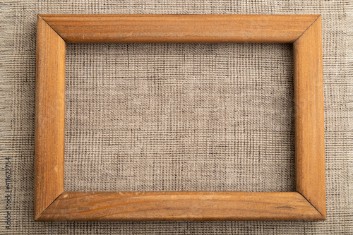 Wooden frame on smooth brown linen tissue. Top view, natural textile background.