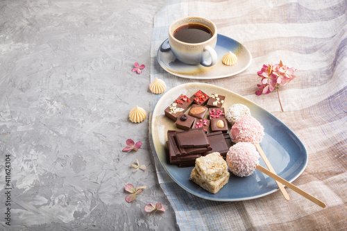 A pieces of homemade chocolate with coconut candies and a cup of coffee on a gray concrete background. side view, copy space.
