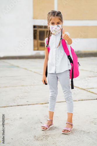 Little girl showing thumbs up with face mask after schhol  photo