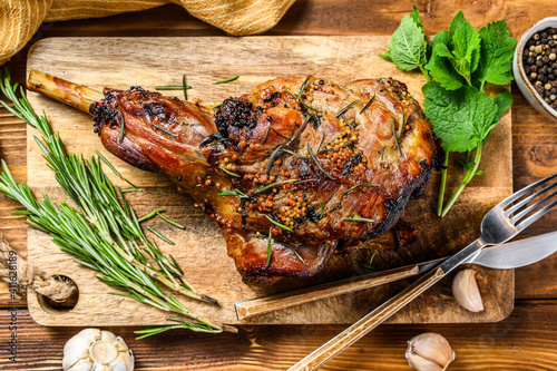 Roasted goat leg with herbs. Farm meat. Wooden background. Top view. Copy space photo