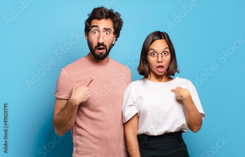 young couple looking shocked and surprised with mouth wide open, pointing to self photo