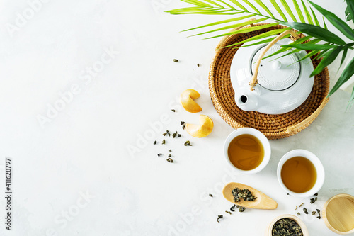 Asian tea concept, two white cups of tea and teapot surrounded with green tea dry leaves view from above, space for a text on white background