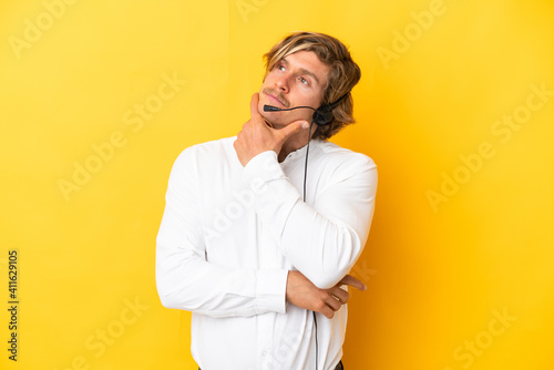 Telemarketer man working with a headset isolated on yellow background having doubts