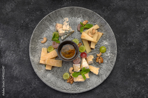 Cheese plate  assorted cheeses with mint  candied fruit  honey and cookies  on a  plate  on a dark background