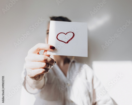 Close-up of a woman's manicured hands holding a drawing of a red heart.Happy Valentine's Day. Love, friendship, and a declaration of love.The concept of heart health and organ donation