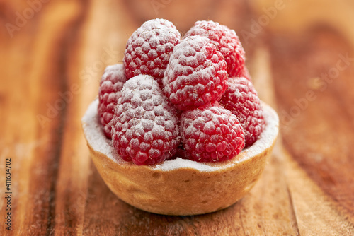 Appetizing raspberry tart with icing sugar on a sponge cake base on a wooden table.