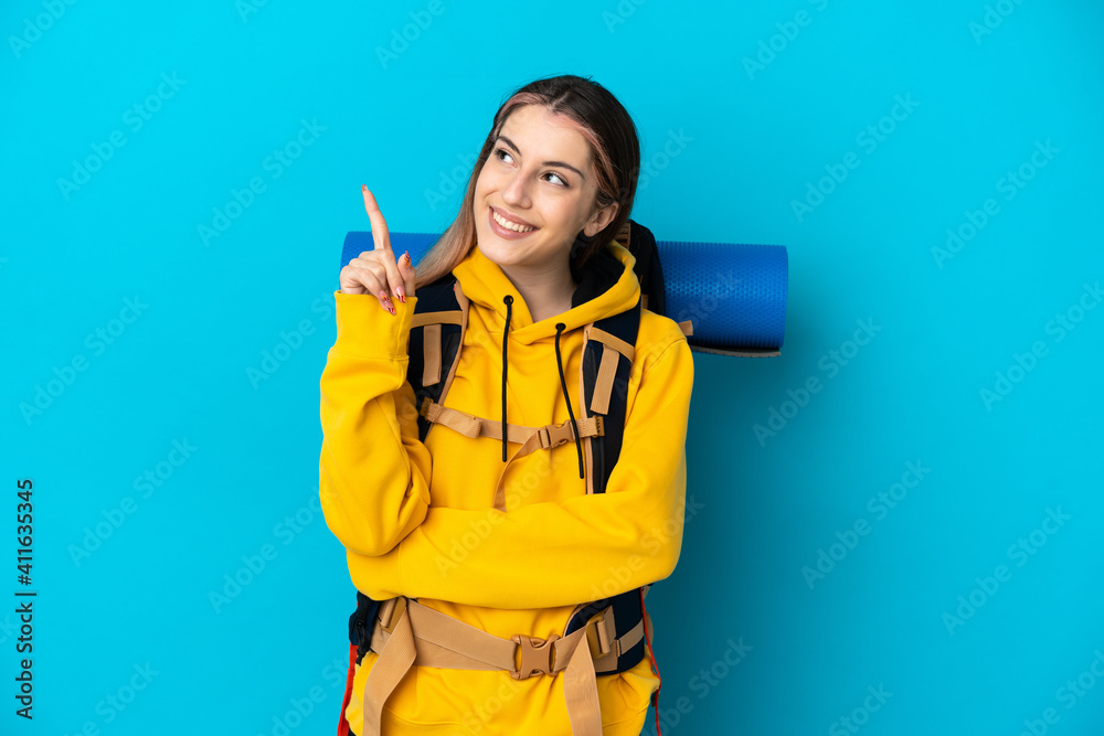 Young mountaineer woman with a big backpack isolated on blue background pointing up a great idea Young mountaineer woman with a big backpack isolated on blue background pointing up a great idea