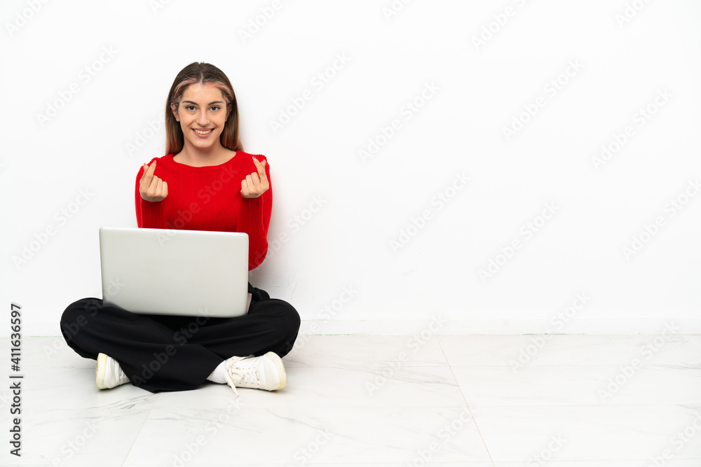 Young caucasian woman with a laptop sitting on the floor making money gesture Young caucasian woman with a laptop sitting on the floor making money gesture