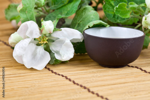 Green tea in a ceramic cup with branches of blossoming apple tree on a bamboo background. Spring background.