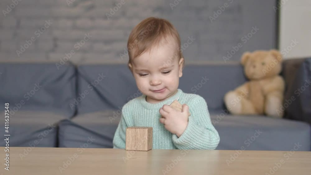 Pretty happy little girl rejoicing playing with wooden cubes standing near table Pretty happy little girl rejoicing playing with wooden cubes standing near table