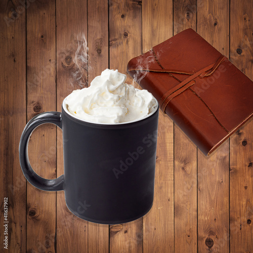 Black coffee cup mockup with whipped cream with leather journal on wood background with room for text.