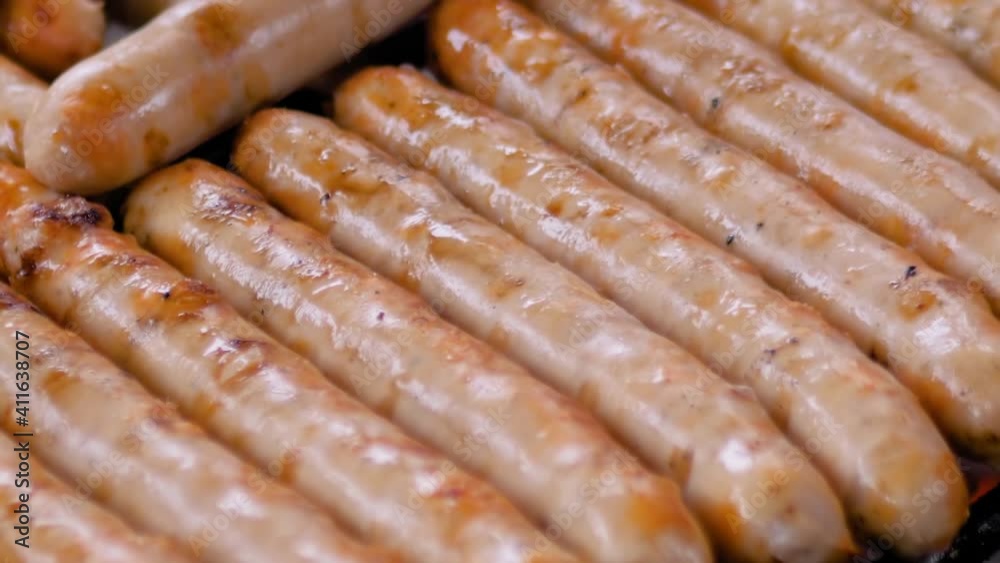 Chef grilling fresh meat sausages on hanging grill at summer local food market - slow motion, close up macro view. Outdoor cooking, barbecue, gastronomy, cookery and street food concept